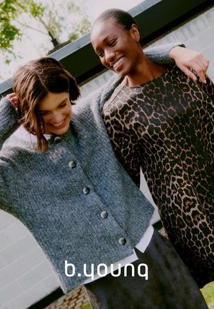 Grauer, gestrickter Cardigan mit runden Knöpfen und lässiger Passform, kombiniert mit einem langärmeligen Oberteil im Leopardenmuster. Beide Modelle stehen nahe beieinander.