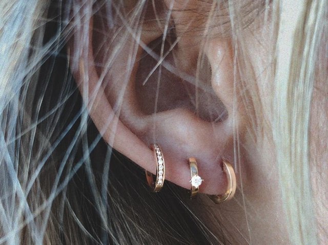 Τρία χρυσά σκουλαρίκια κρίκοι φορεμένα στο αυτί: ένα με μια διαμαντένια λεπτομέρεια, ένα με ενσωματωμένα κρύσταλλα και ένα με απλό και λείο σχέδιο.