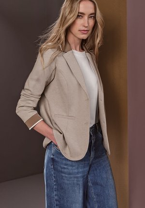 Beige blazer met lichtbruine accenten, twee voorkruiden, gecombineerd met een witte top en lichtblauwe wijde jeans, gladde textuur en aansluitend ontwerp.