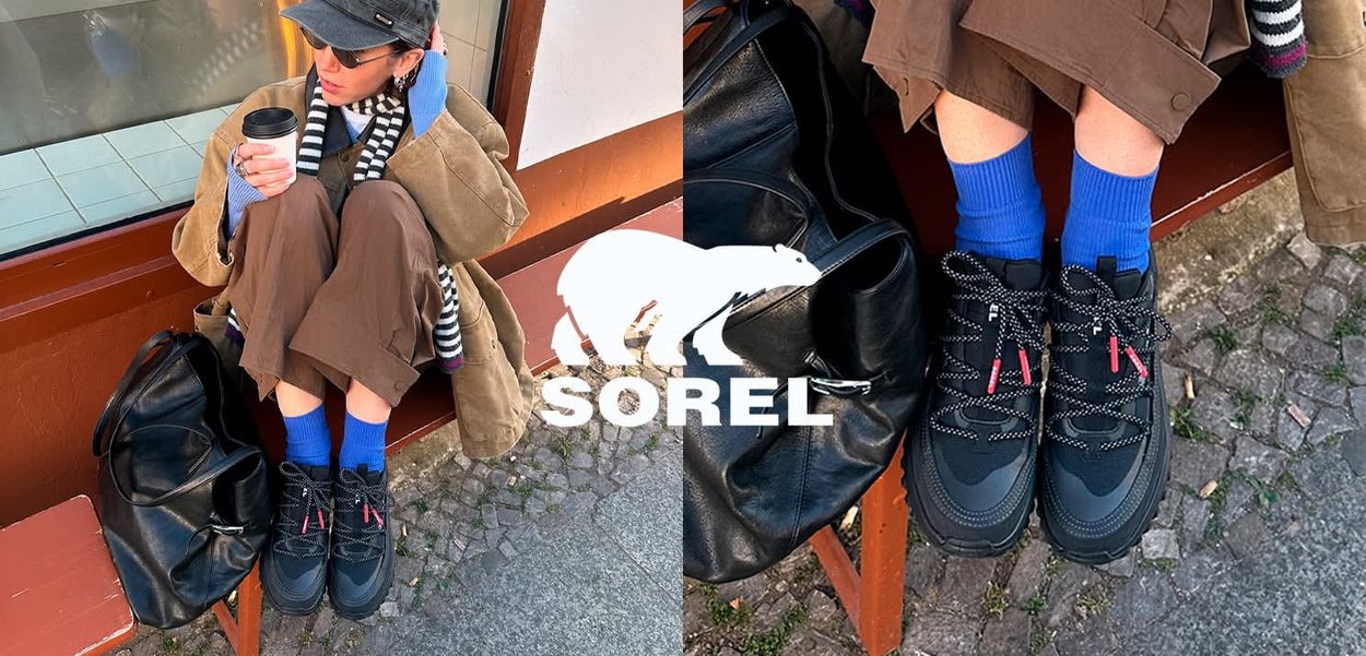 Personne en pantalon marron, chaussettes bleues et baskets noires assise sur un banc tenant une tasse de café, avec un sac noir à côté.