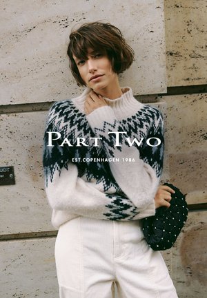 Maglione a maglia con base bianca, motivi geometrici neri e grigi, colletto a costine. Abbinato a pantaloni in velluto a coste chiari e una borsa testurizzata.