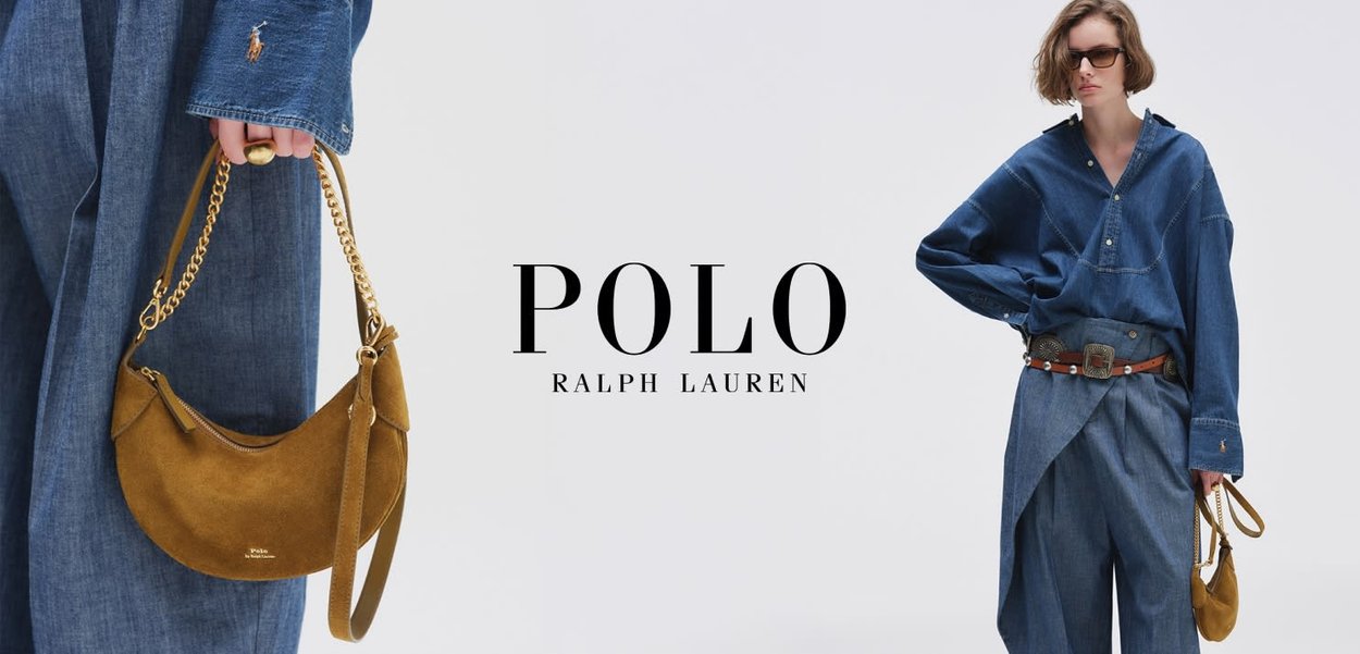 Persoon draagt een oversized denim shirt en broek met riem, en houdt een kleine bruine suède handtas met gouden kettingband vast.