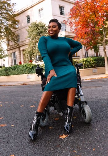 Teal ribbat klänning med långa ärmar, svarta högklackade stövlar, sittande i en rullstol med modern design, mot en bakgrund av höstl övd.