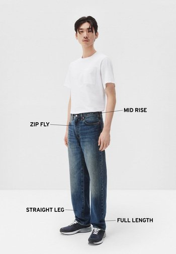 Jeans azul de altura media con cremallera, pierna recta y diseño de longitud completa, combinados con una camiseta blanca de manga corta y zapatillas oscuras.