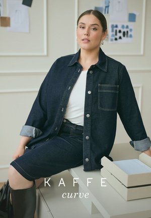 Dark denim jacket with a button-down design, chest pocket, and rolled sleeves, paired with a fitted denim skirt and a white t-shirt.