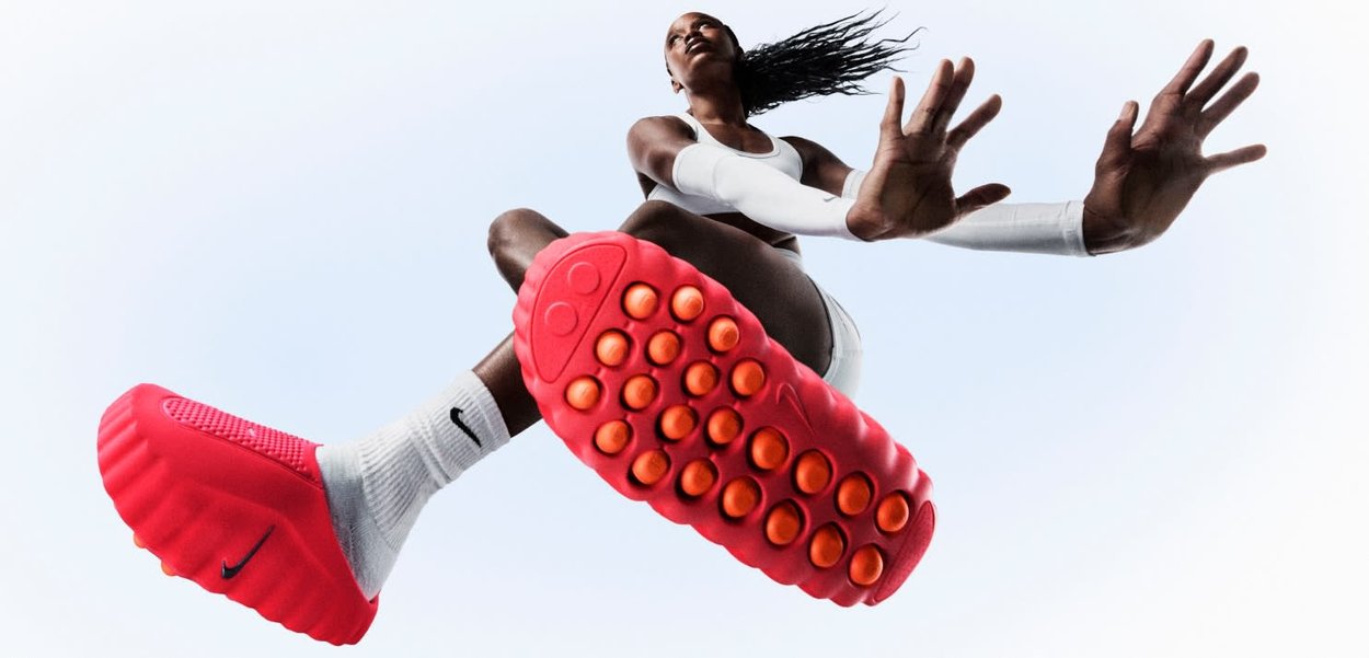 Nike-sneaker met een opvallende rode zool met afgeronde oranje noppen. Bovenwerk met een gestructureerd ontwerp, gecombineerd met witte sportkleding en sokken.