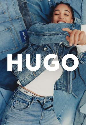 Lichtblauwe denimjas en -spijkerbroek, met logo-accenten. Model draagt een witte top met een zichtbare logo-broekband. Tekstoverlay: "HUGO."