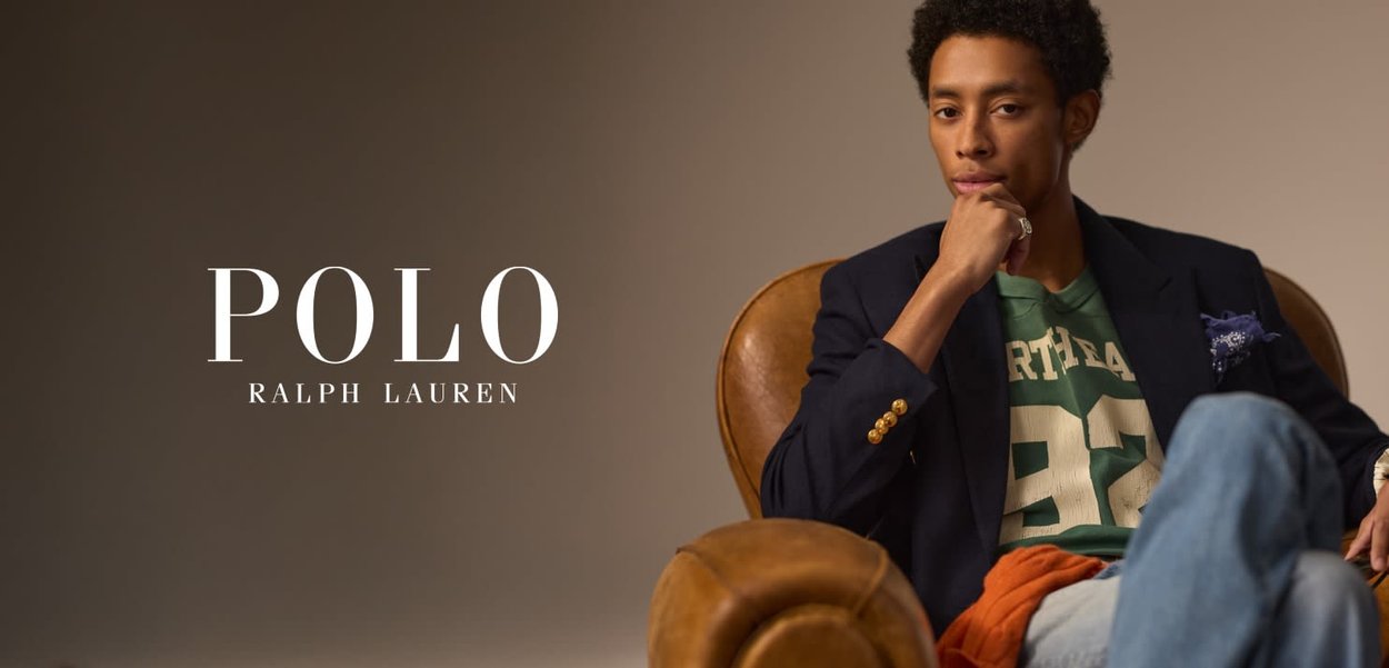 Blazer bleu marine, t-shirt graphique vert avec écriture blanche, jeans en denim, assis sur un fauteuil en cuir marron, pose réfléchie, avec un mouchoir de poche à motif.