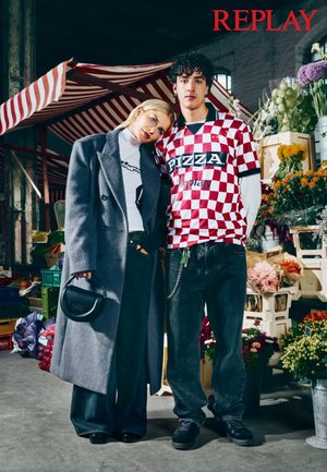 To modeller står i et blomstrende marked. Kvinden har på en grå frakke og en hvid turtleneck; manden har på en rød og hvid ternet skjorte.