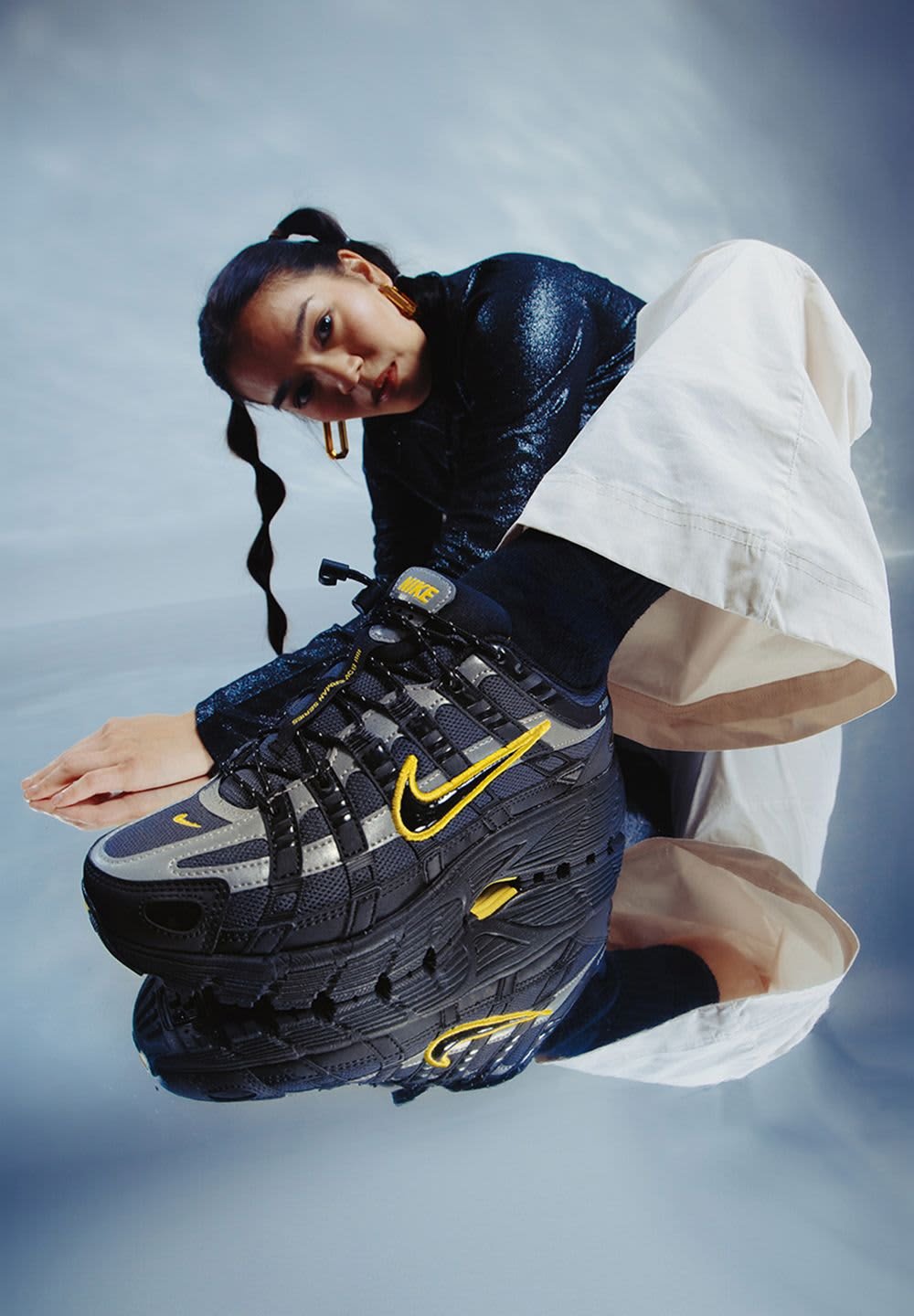 Black and grey Nike sneaker with yellow accents, mesh texture, prominent lacing system, and a thick sole, set against a reflective surface.