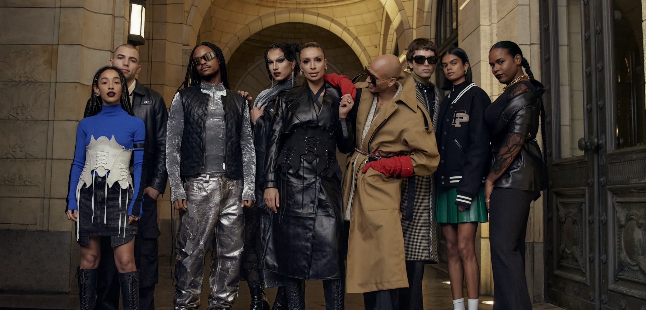 Negen individuen in verschillende outfits: leer, denim en gestructureerde stukken; kleuren zijn zwart, blauw, zilver en tan. Unieke ontwerpen bevatten veters en patronen.