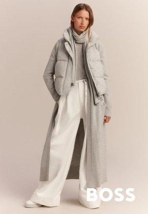 Grijze gewatteerde vest over een aansluitende grijze sweater, gecombineerd met brede witte broeken. De outfit heeft een lange grijze cardigan en een bijpassende sjaal.