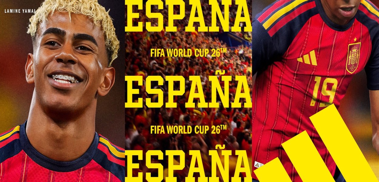 Joven futbolista con camiseta roja de España, número 19, pelo rubio rizado, sonriendo, con una multitud y el texto "ESPANA FIFA WORLD CUP 26" al fondo.