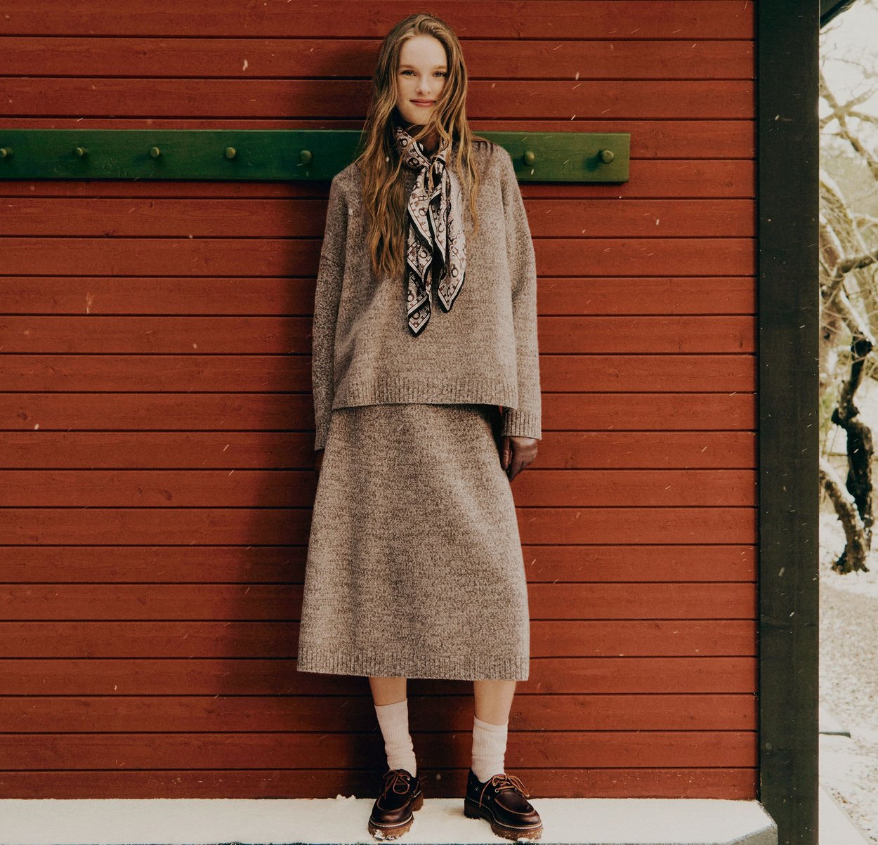 Ljusgrå stickad tröja och matchande midikjol, accentuerade med en mönstrad scarf, ihop med bruna skor och krämfärgade strumpor.