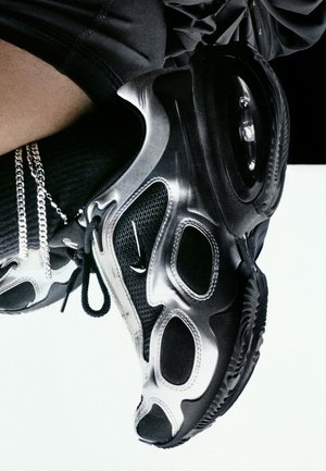 Des baskets Nike noires et argentées présentent un dessus en maille texturée, un amorti d'air surdimensionné et des découpes distinctes sur le côté pour la ventilation.