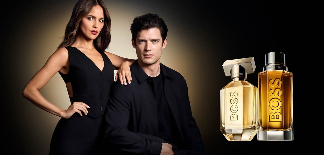 Frau im schwarzen Kleid steht mit der Hand auf der Schulter eines sitzenden Mannes; zwei BOSS-Parfümflaschen sind neben ihnen vor dunklem Hintergrund zu sehen.