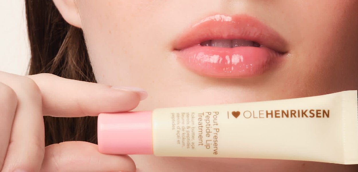 Tubo di trattamento labiale a peptide con corpo crema chiaro e tappo rosa. Labbra lisce e lucide in primo piano su uno sfondo chiaro.