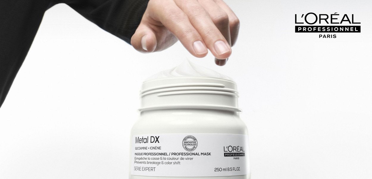 Hand, die nach weißer Creme in einem offenen Glas mit der Aufschrift Metal DX Professional Mask von L'Oréal Professionnel Paris, 250 ml, greift.