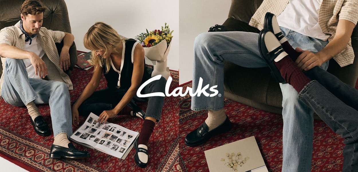 Mocassins bicolores noir et blanc à finition brillante, portés avec des chaussettes beiges et bordeaux. Tenue décontractée présentée sur un tapis à motifs.