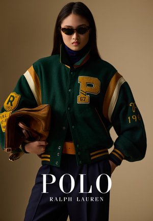 Grüne Woll-Baseballjacke mit gelben und cremefarbenen Akzenten, Buchstabe "P" und Jahreszahlen-Patches, kombiniert mit dunklen Hosen und einer braunen Lederhandtasche.
