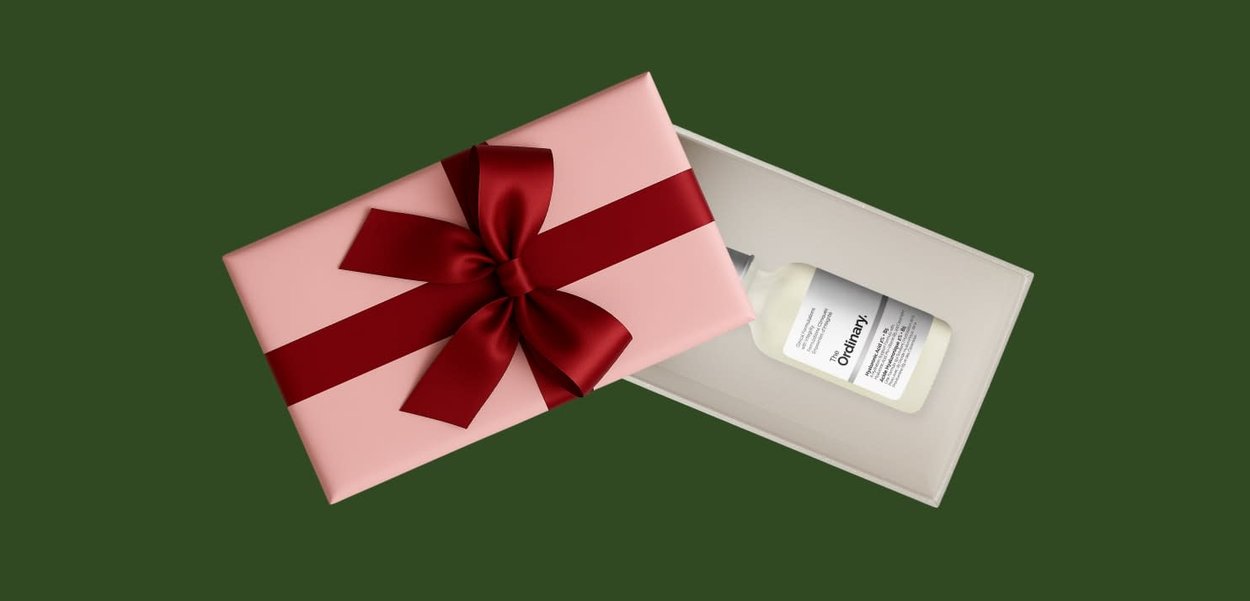 Cadeaubox met roze verpakking en rode strik, geopend om een flesje van The Ordinary huidverzorgingsproduct te tonen.