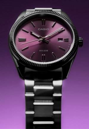 Reloj de pulsera Casio con esfera morada, índices horarios plateados, fecha mostrando 17 y pulsera metálica plateada sobre fondo morado.