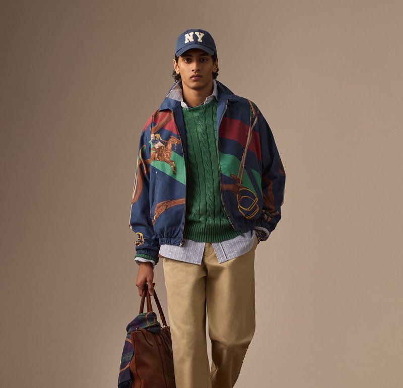Veste bomber multicolore avec imprimé de cheval, pull en maille verte, chemise bleu ciel à boutons, pantalon beige clair et sac fourre-tout marron.
