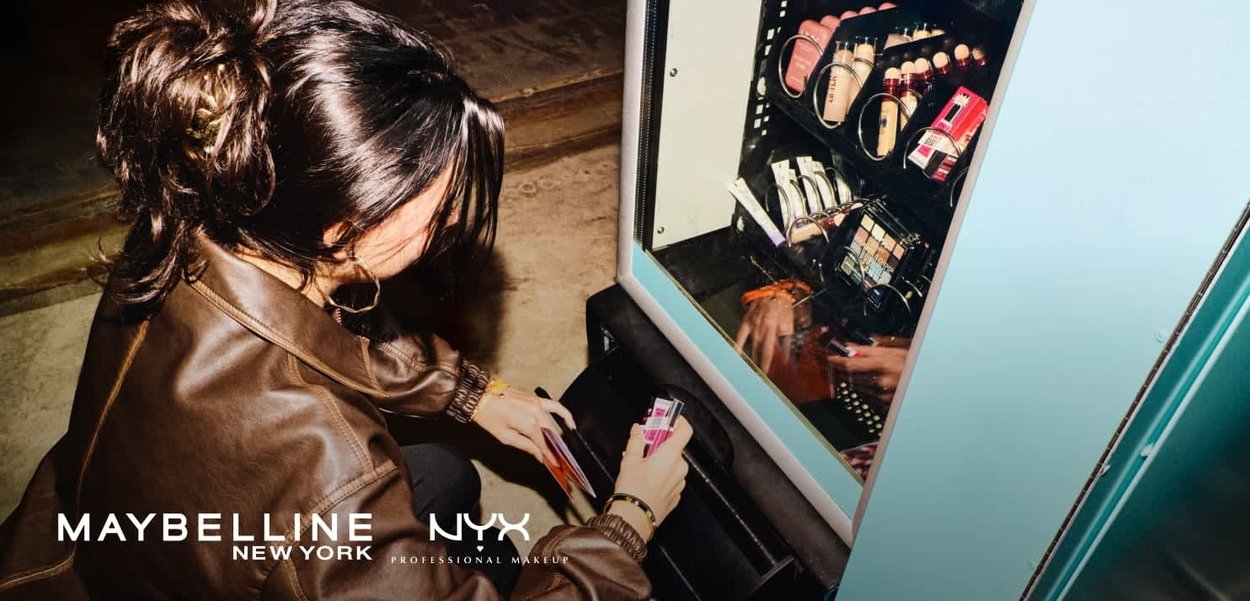 Donna con giacca marrone che seleziona prodotti per il trucco da un distributore automatico rifornito di vari cosmetici.