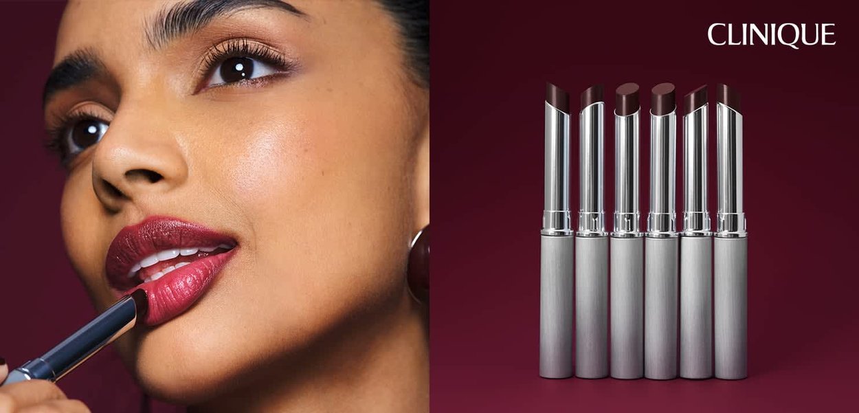 Donna che si applica un rossetto rosso scuro con sei rossetti simili esposti accanto a lei su uno sfondo bordeaux.