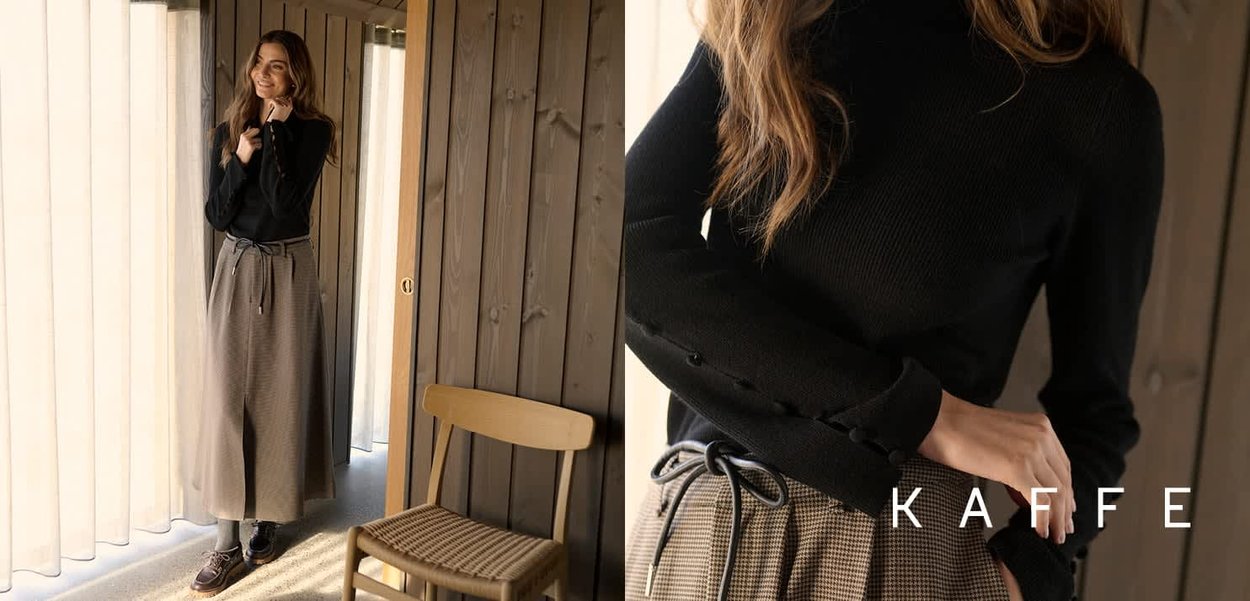 Musta ribbituulepaita, jossa on napit yksityiskohtina, yhdistettynä beigeen ruutukuosisiseen maksihameeseen, jossa on solmittava vyö. Puulaitta taustalla.