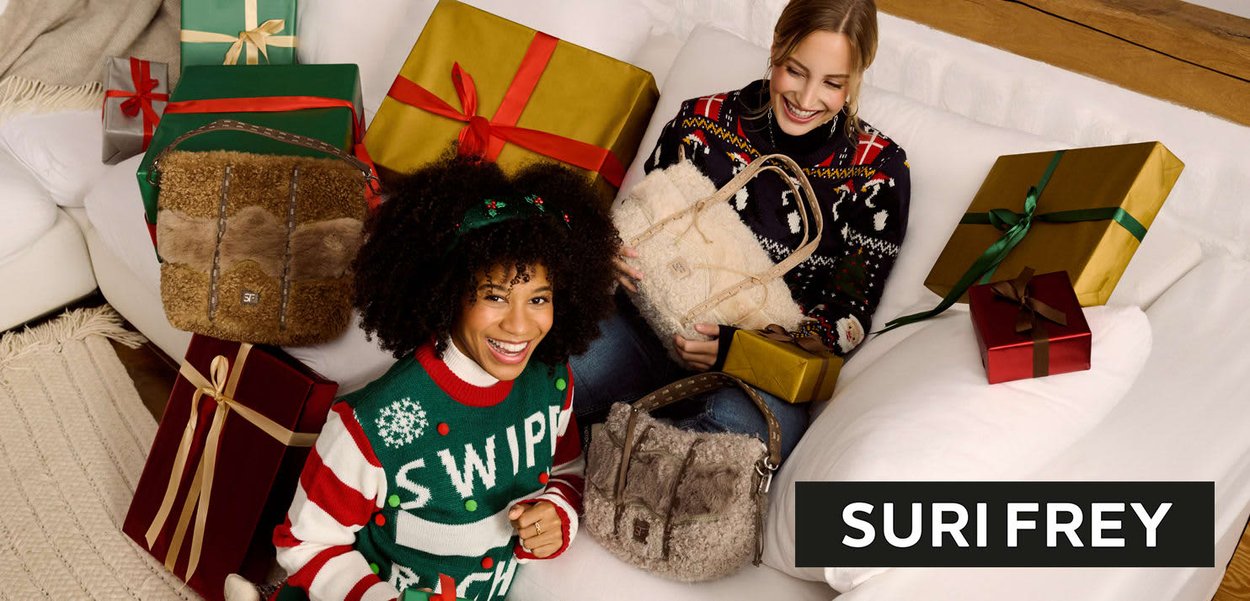 Zwei Frauen sitzen auf einem weißen Sofa mit farbenfroh eingepackten Geschenken. Die eine hält eine beige, flauschige Tasche, die andere eine cremefarbene Tasche. Sie tragen Weihnachts-Pullover.