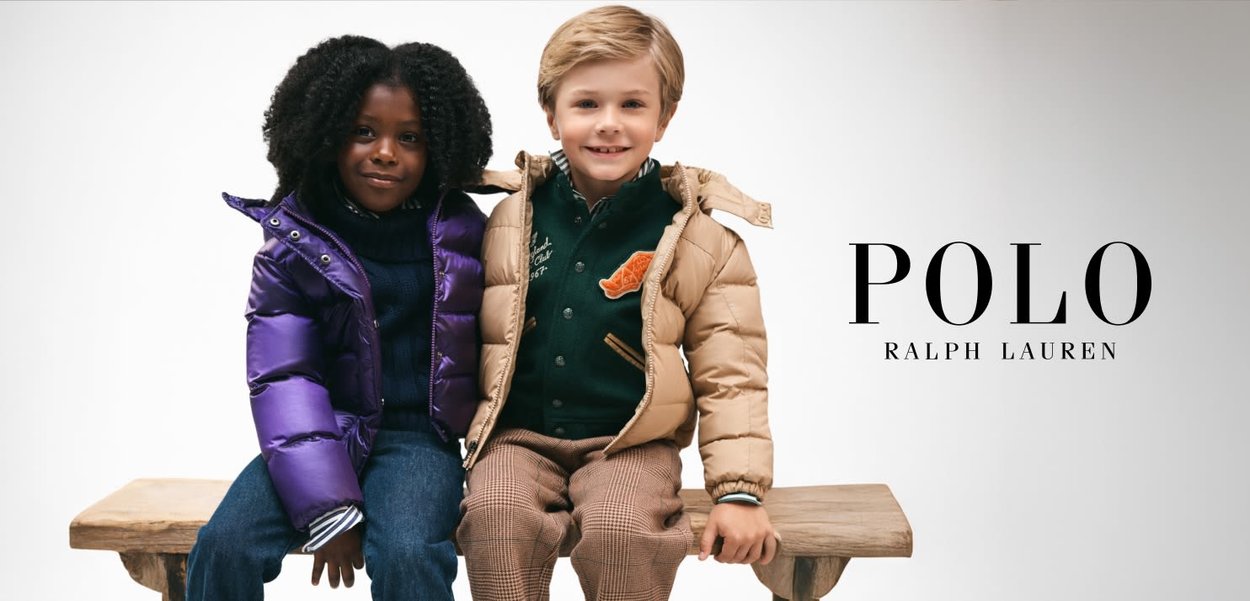 Twee kinderen zitten op een houten bankje, gekleed in winterjassen, met het POLO Ralph Lauren-logo op een witte achtergrond.