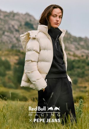 Gewatteerd jack in crème met een hoge kraag en capuchon, voorzien van doorgestikte secties. Draagt over een zwarte trui en losse zwarte broek.