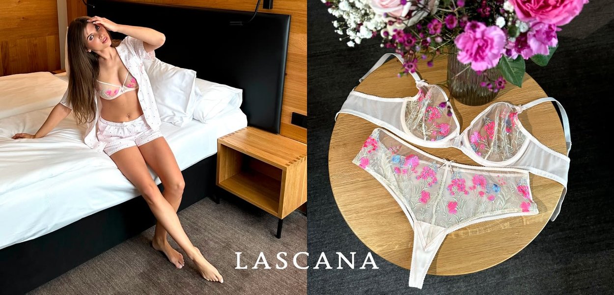 Frau in floraler Unterwäsche und durchsichtigem Morgenmantel posiert auf dem Bett; passender bestickter BH und Unterhose auf einem runden Holztisch mit Blumen präsentiert.
