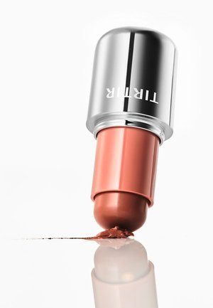 Lippenstift met een zilveren dop met het label "TIRTIR" die een koraalkleur aanbrengt, gereflecteerd op een glanzend wit oppervlak.