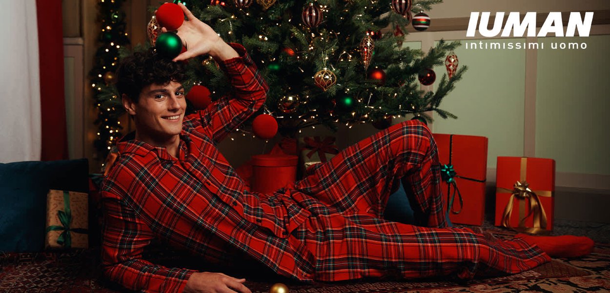 Pigiama a quadri rossi con vestibilità comoda, maniche lunghe e pantaloni. Sullo sfondo un albero di Natale decorato e regali incartati.