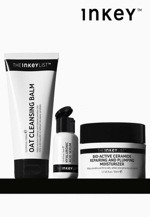 Tre hudplejeprodukter på en hvid baggrund: en tube havre-rensesalve, et serum i en lille flaske og en krukke fugtighedscreme, alle i elegant emballage.