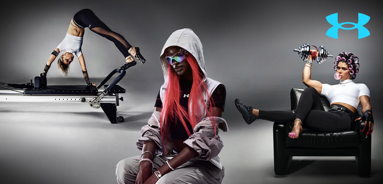 Deux femmes présentant des équipements Under Armour ; l'une fait un équilibre sur les mains sur un appareil de fitness, l'autre est accroupie, portant des lunettes de soleil et une capuche.