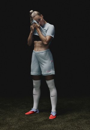 Completo da calcio azzurro chiaro con maniche corte, pantaloni coordinati e accenti rosa. Calze bianche al ginocchio e scarpini da calcio arancioni brillanti.