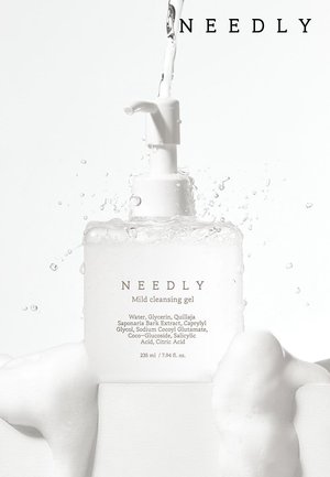 Bouteille transparente avec un distributeur à pompe blanc, contenant un gel nettoyant doux. L'étiquette présente du texte et des ingrédients dans une police simple. Bulles et éclaboussures d'eau tout autour.