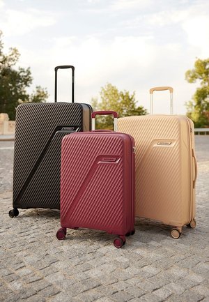 Drei Gepäckstücke: schwarz, kastanienbraun und beige. Jedes hat ein strukturiertes diagonales Rippmuster, ausziehbare Griffe und glatte Rollen.