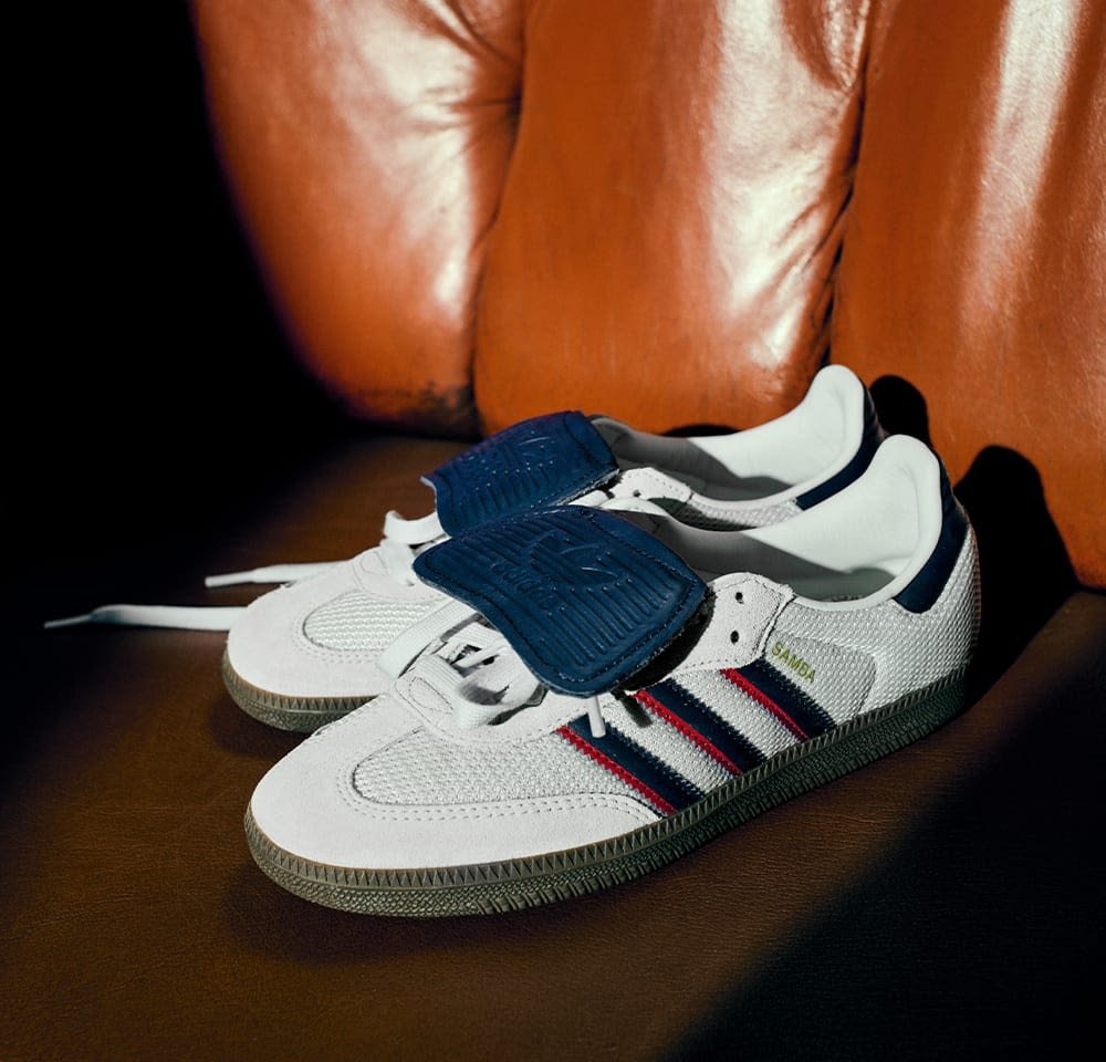 Balti tinkliniai sportbačiai su tamsiai mėlynomis akcentais ir raudonomis juostelėmis, turintys tekstūruotą tamsiai mėlyną dirželį. Guma neišslystančiu padu su raštu.