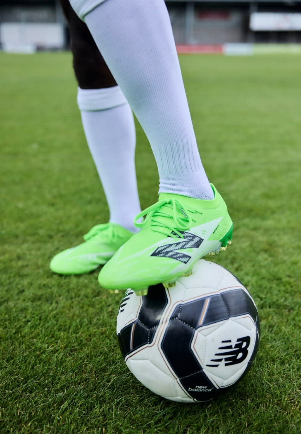 Des crampons de soccer verts sur un ballon de soccer noir et blanc, posé sur de l'herbe. Les crampons présentent un design texturé et sont maintenus par des lacets.
