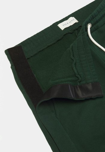 Mörkgröna shorts i mjukt tyg, med elastiskt midjeband, snörning och en sidoflik med svart kardborrestängning.