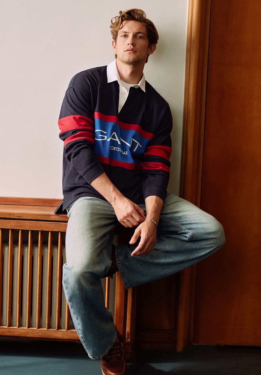 Long-sleeve navy polo with red and blue stripes; GANT logo on front. Worn with light blue baggy jeans; sitting on a wooden bench.