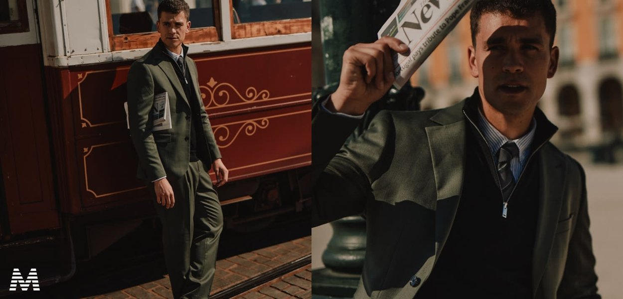 Dunkelgrüner Anzug im Slim Fit, über einem blau-weiß gestreiften Hemd getragen. Hält eine Zeitung und steht neben einer historischen Straßenbahn.