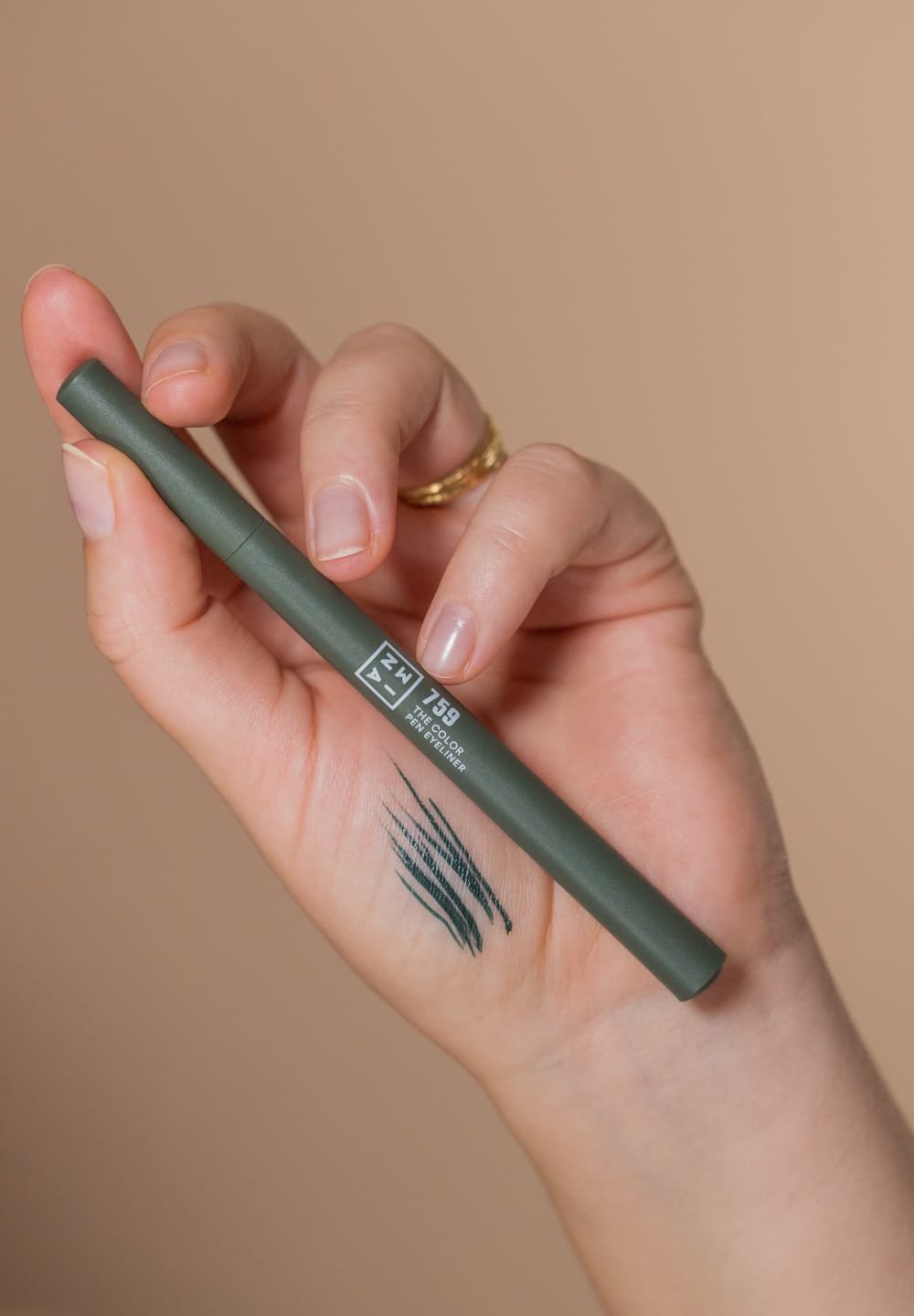 Grønne penneeyeliner holdes i en hånd med en mat finish. Sorte linjer tegnet på huden nedenfor, der fremhæver en flydende påføring.