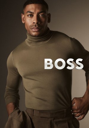 Olivgrüner Rollkragenpullover mit eng anliegendem Design und gerippten Bündchen, kombiniert mit tanfarbenen Hosen. Das "BOSS"-Logo ist prominent sichtbar.