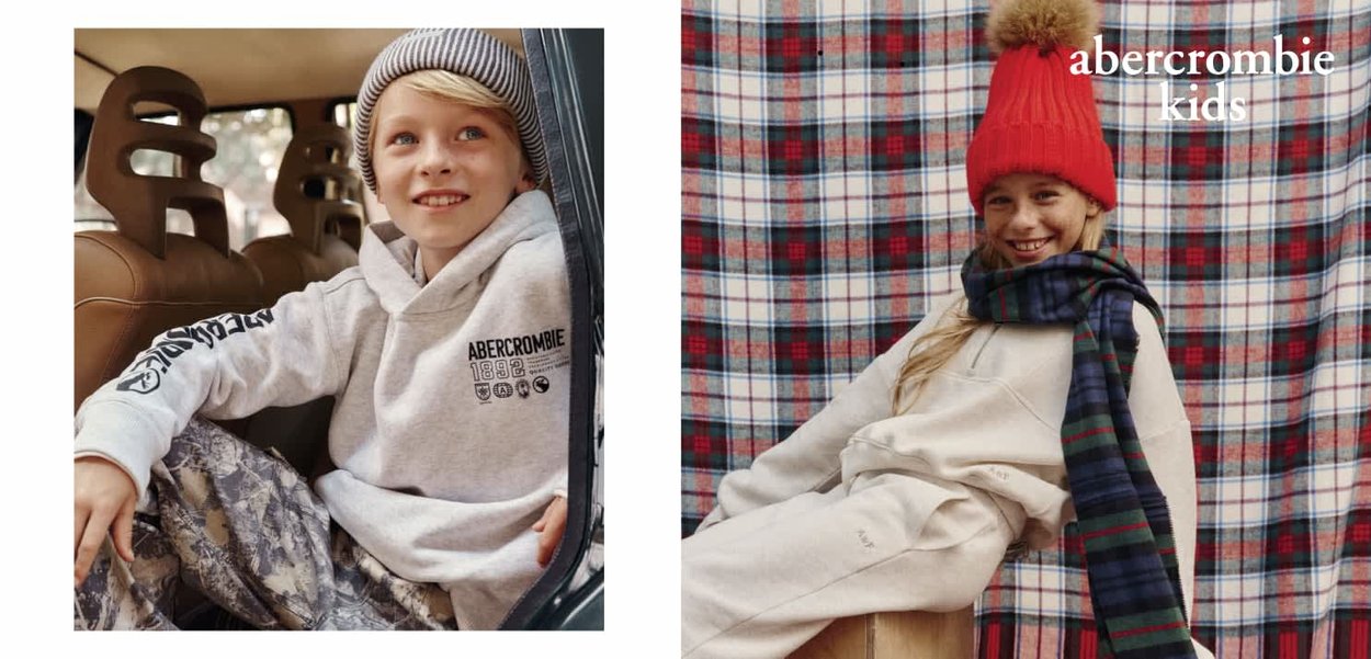 Dwoje dzieci nosi codzienne stroje. Jedno w szarej bluzie z kapturem i spodniach w kamuflażu, drugie w beżowej bluzie z kapturem, czerwonej dzianinowej czapce i kraciastej szaliku, na tle w kratę.