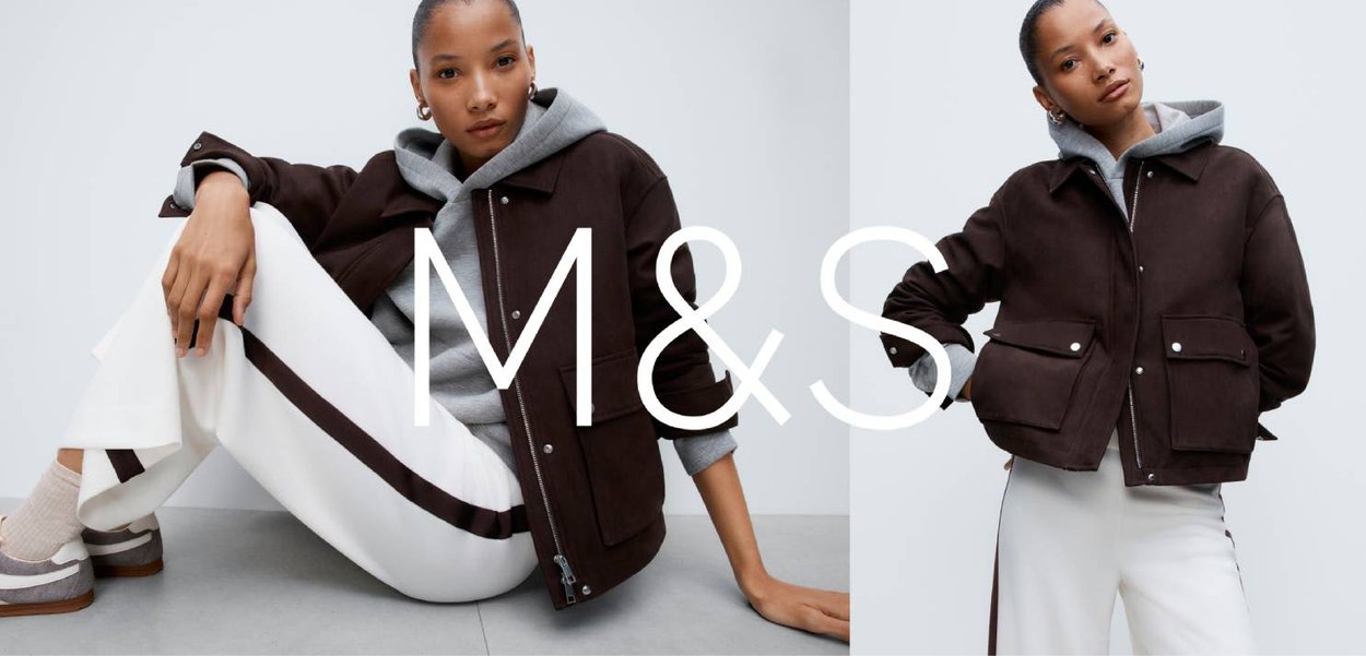 Brązowa kurtka bombowiec z dwoma przednimi kieszeniami, szara bluza z kapturem pod spodem, w połączeniu z białymi spodniami z ciemnymi paskami.